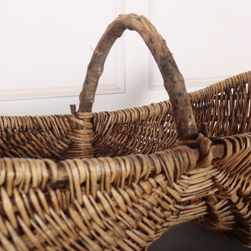 A large woven wicker twin harvest basket featuring a bentwood central handle and faded red painted marks on the natural exterior. View V