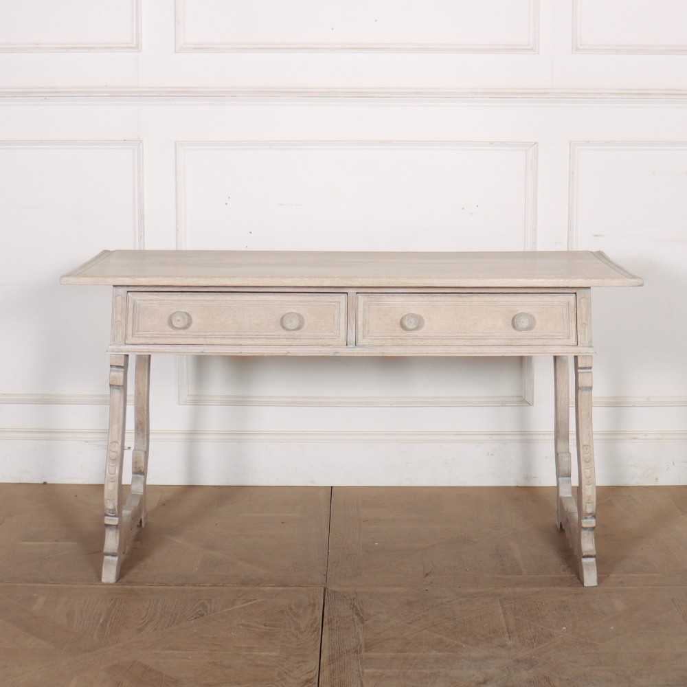 A bleached oak Spanish server table featuring two frieze drawers with round wooden knobs, resting on carved trestle-style end supports.