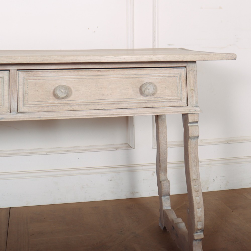 A bleached oak Spanish server table featuring two frieze drawers with round wooden knobs, resting on carved trestle-style end supports. View IV