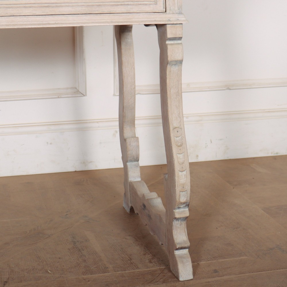 A bleached oak Spanish server table featuring two frieze drawers with round wooden knobs, resting on carved trestle-style end supports. View V