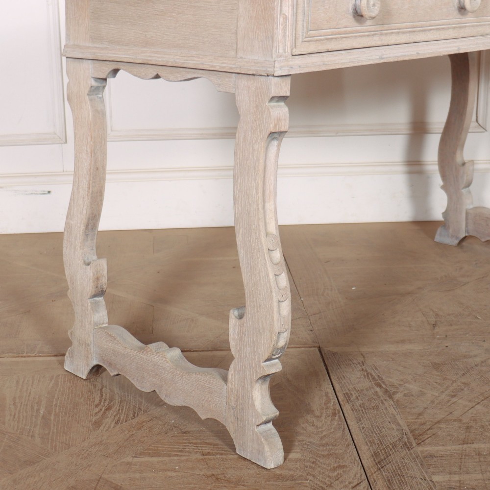 A bleached oak Spanish server table featuring two frieze drawers with round wooden knobs, resting on carved trestle-style end supports. View VII