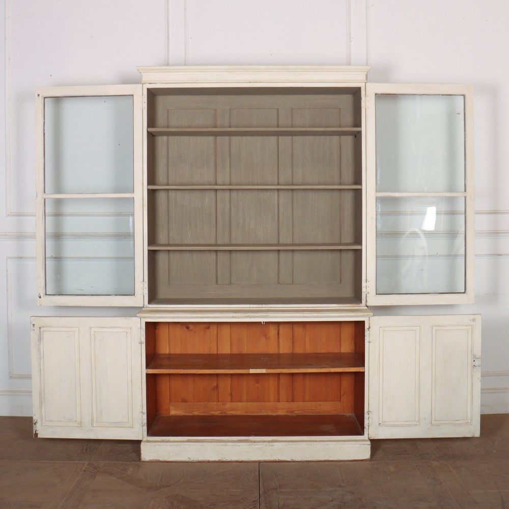 A tall 19th-century painted wooden bookcase featuring a cream exterior, two upper glazed doors revealing a grey interior with shelves, and a double-panelled lower cupboard base. View VII