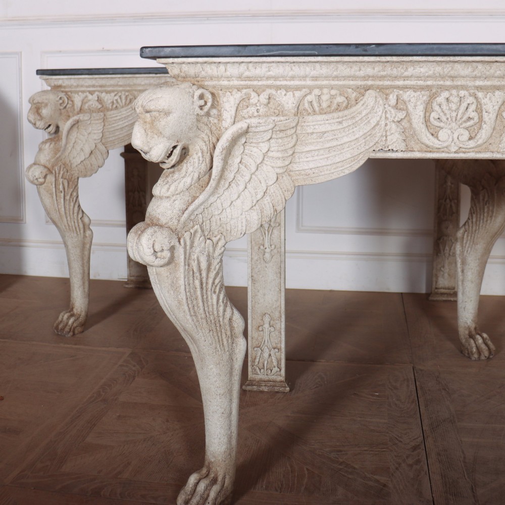 A pair of large off-white painted console tables featuring carved winged lion monopodium supports, anthemion friezes, and dark grey tops. View II