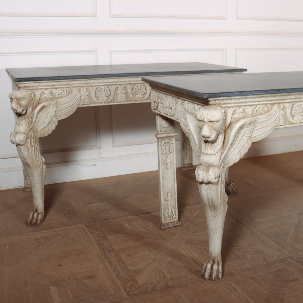 A pair of large off-white painted console tables featuring carved winged lion monopodium supports, anthemion friezes, and dark grey tops. View VII