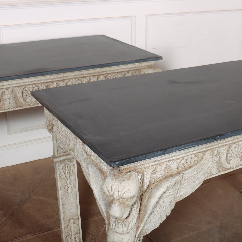 A pair of large off-white painted console tables featuring carved winged lion monopodium supports, anthemion friezes, and dark grey tops. View X