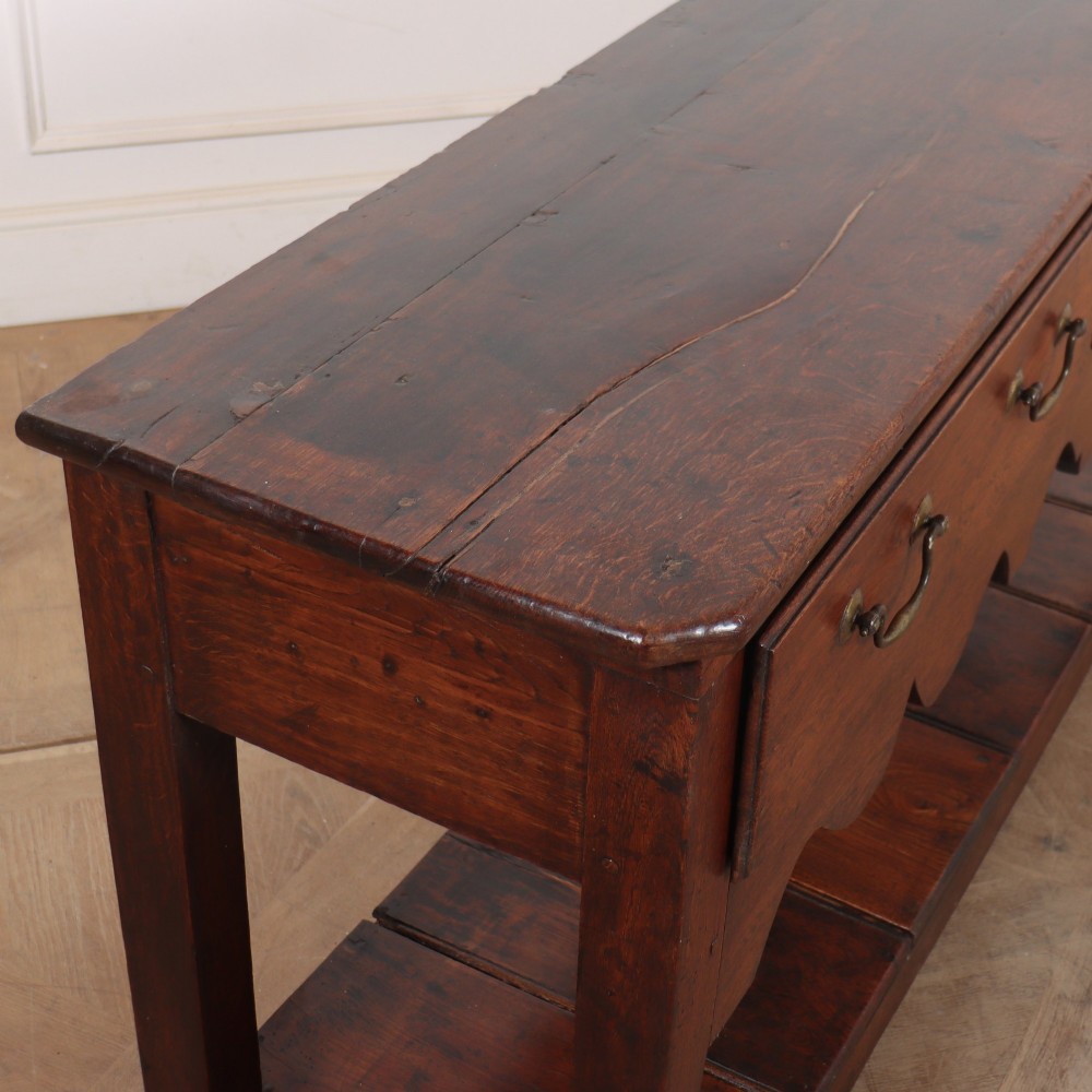 An antique dark oak Welsh dresser base featuring two broad drawers with brass handles, a decorative scalloped apron, and an open lower pot board shelf. View IX