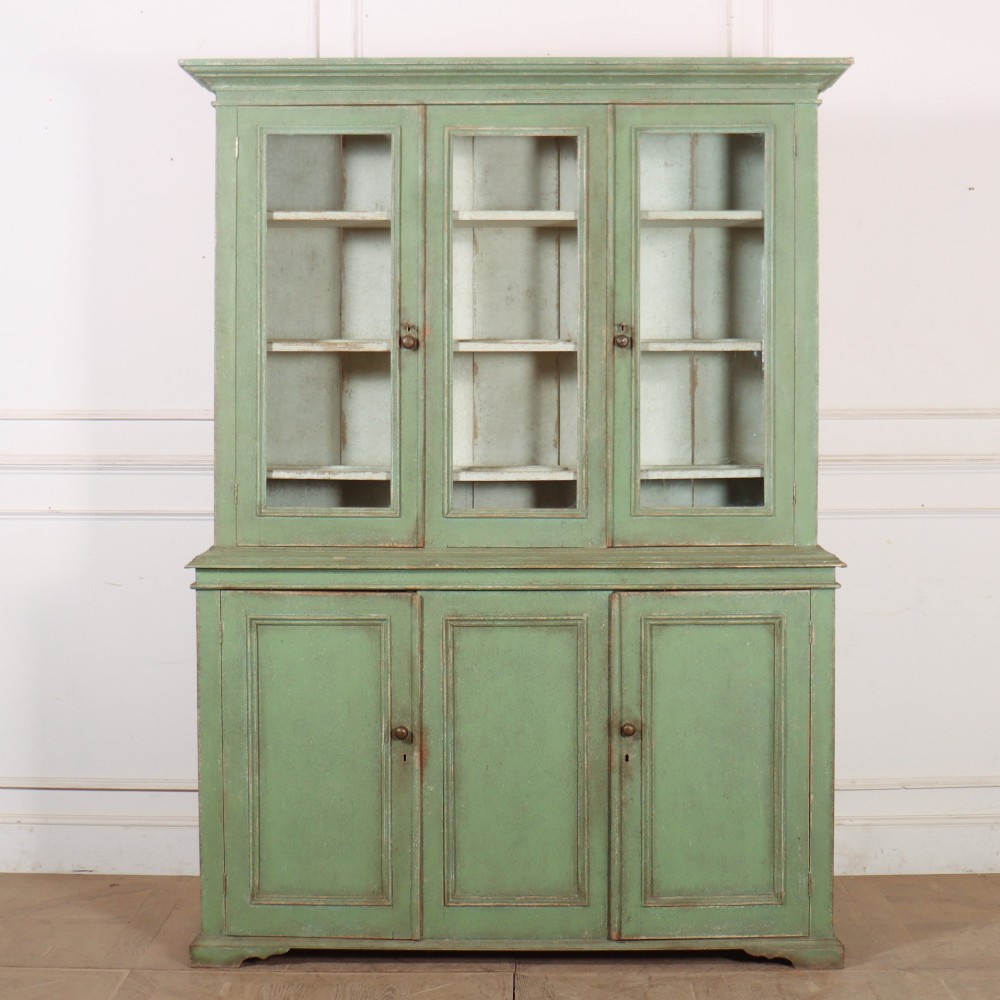 A two-part antique green painted wood kitchen dresser featuring a three-door glazed upper cabinet and three panelled cupboard doors below.