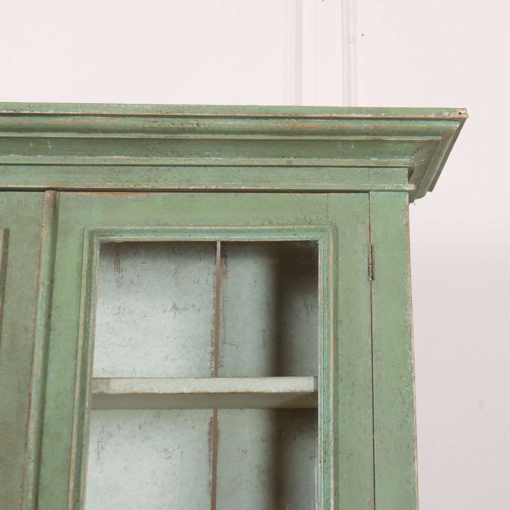 A two-part antique green painted wood kitchen dresser featuring a three-door glazed upper cabinet and three panelled cupboard doors below. View VII