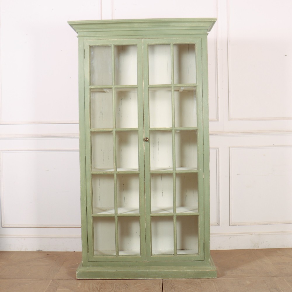 A tall 19th-century English painted sage green glazed display bookcase with two glass panel doors and an off-white interior.