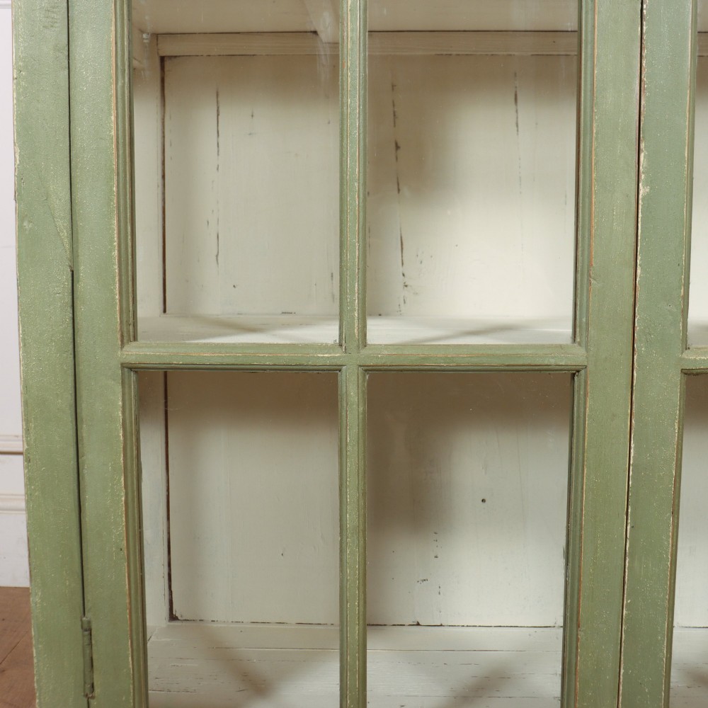 A tall 19th-century English painted sage green glazed display bookcase with two glass panel doors and an off-white interior. View VI