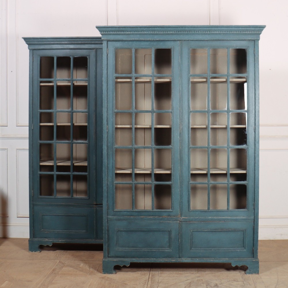 A pair of tall English glazed library bookcases painted in a muted teal blue finish with contrasting light interior shelves and glass grid doors.