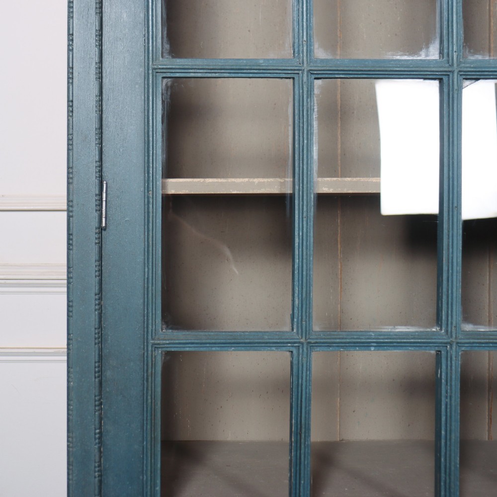 A pair of tall English glazed library bookcases painted in a muted teal blue finish with contrasting light interior shelves and glass grid doors. View XII