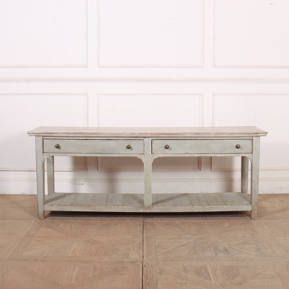An English painted wooden potboard dresser base with a scrubbed timber top, two drawers, turned legs, and an open slatted lower shelf.