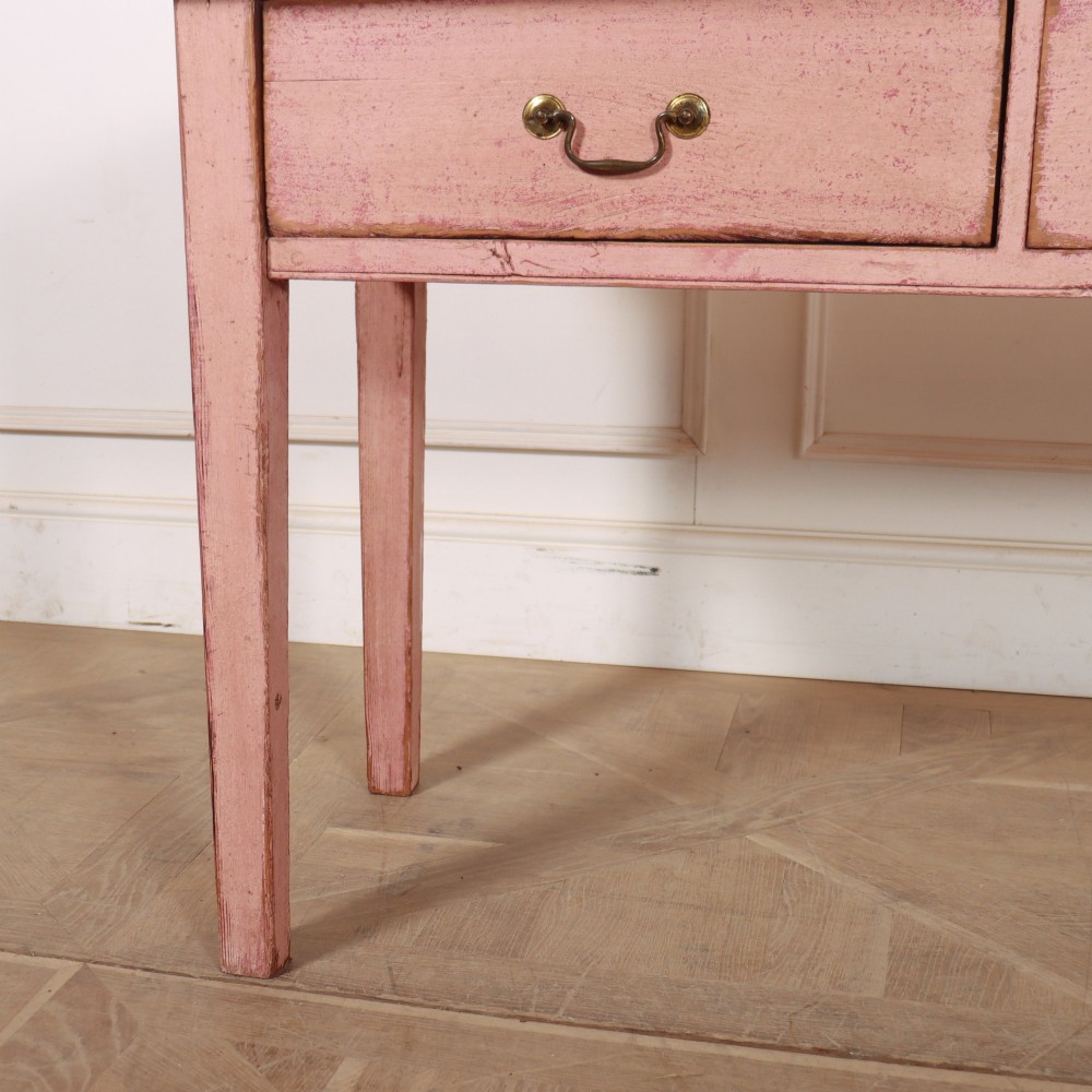 An antique English wooden server featuring a scrubbed natural timber top, a distressed pink painted frame, three drawers with brass drop handles, and four straight legs. View IV