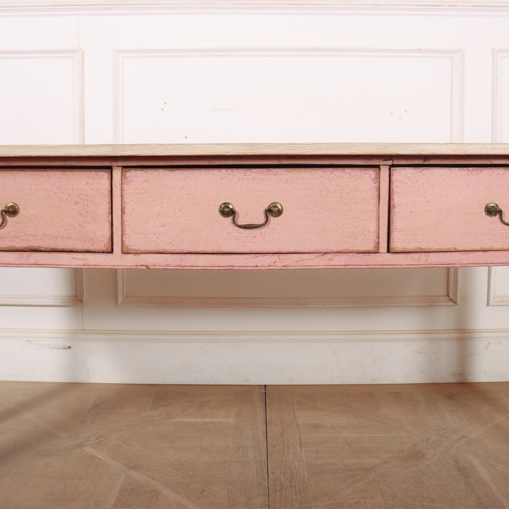 An antique English wooden server featuring a scrubbed natural timber top, a distressed pink painted frame, three drawers with brass drop handles, and four straight legs. View V