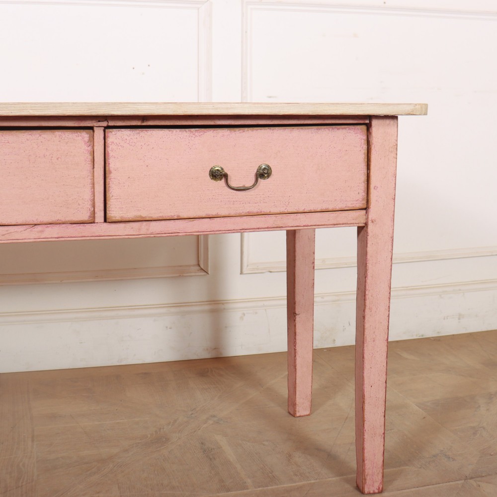 An antique English wooden server featuring a scrubbed natural timber top, a distressed pink painted frame, three drawers with brass drop handles, and four straight legs. View VI