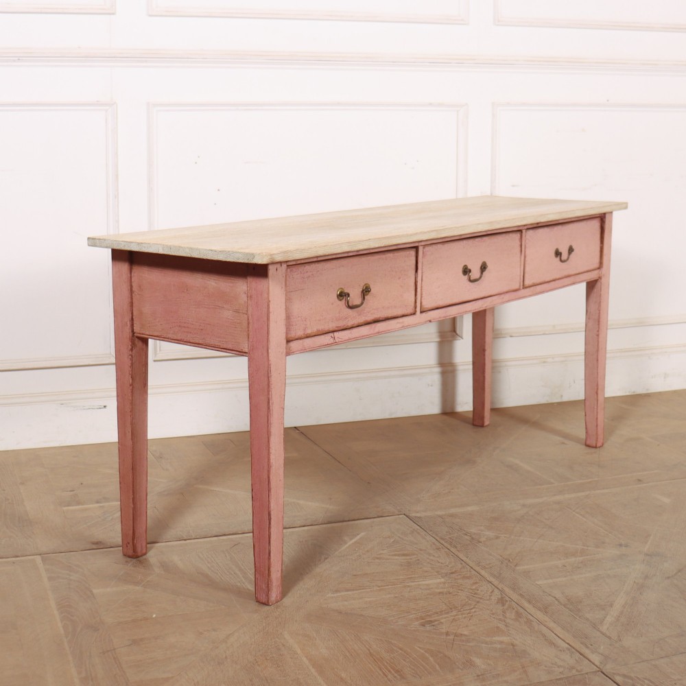 An antique English wooden server featuring a scrubbed natural timber top, a distressed pink painted frame, three drawers with brass drop handles, and four straight legs. View IX