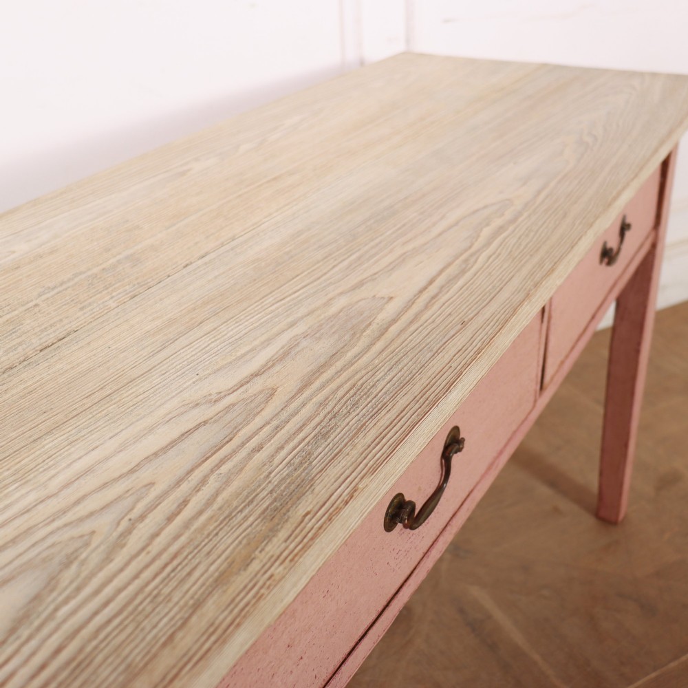 An antique English wooden server featuring a scrubbed natural timber top, a distressed pink painted frame, three drawers with brass drop handles, and four straight legs. View XI
