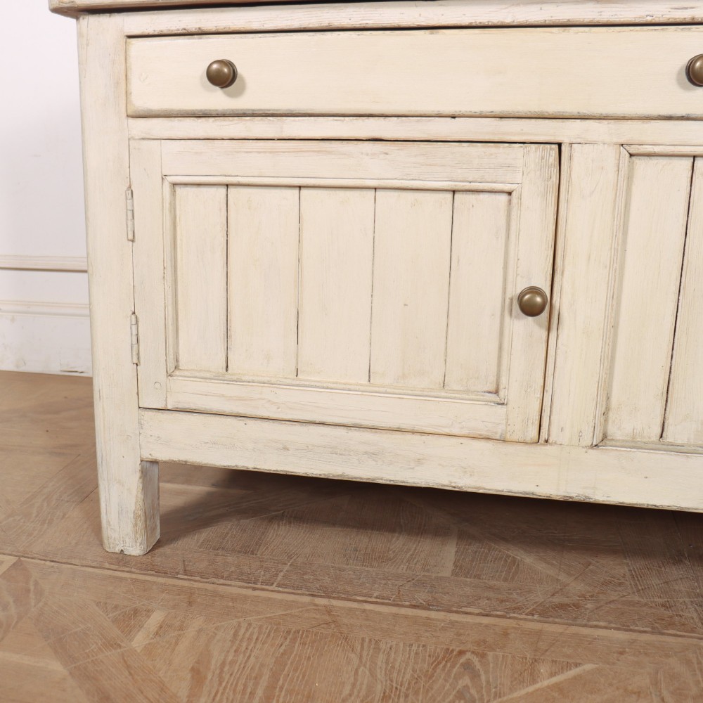 An English painted wood dresser base featuring two long top drawers with brass knob handles above panelled cupboard doors. View III