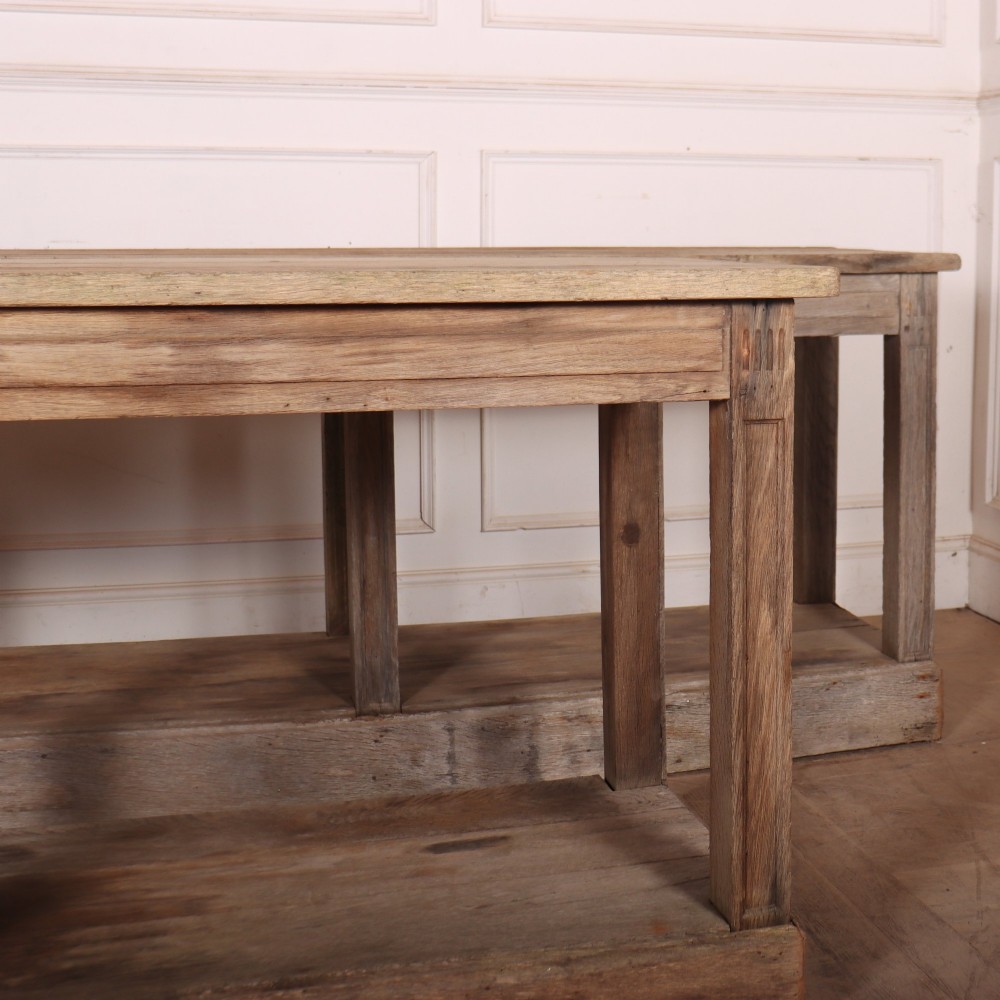 A pair of long rustic wooden French console tables with lower open shelves and weathered pale timber finish. View II