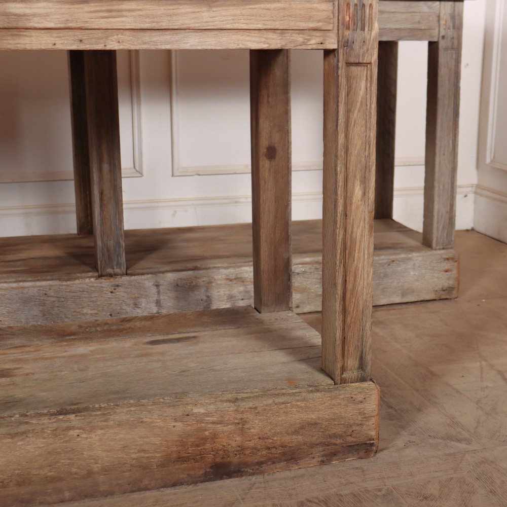 A pair of long rustic wooden French console tables with lower open shelves and weathered pale timber finish. View III