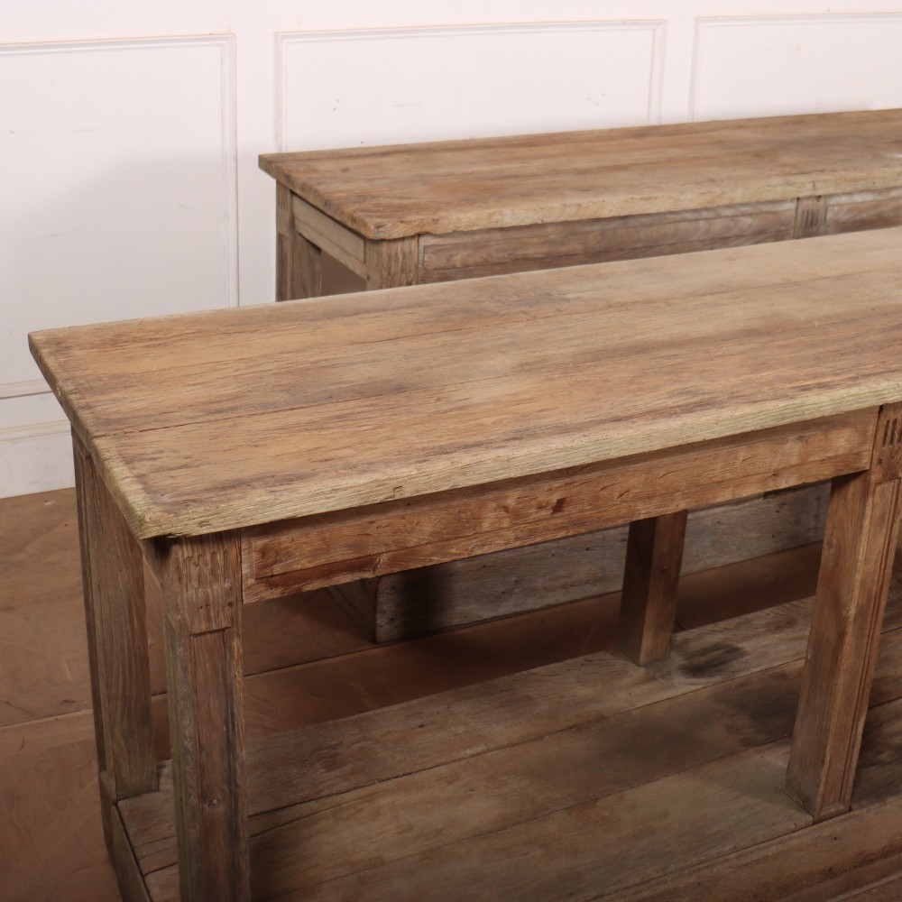 A pair of long rustic wooden French console tables with lower open shelves and weathered pale timber finish. View VI
