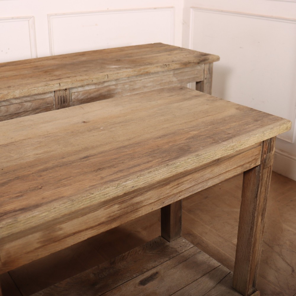 A pair of long rustic wooden French console tables with lower open shelves and weathered pale timber finish. View VII