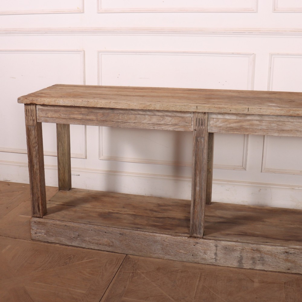 A pair of long rustic wooden French console tables with lower open shelves and weathered pale timber finish. View IX