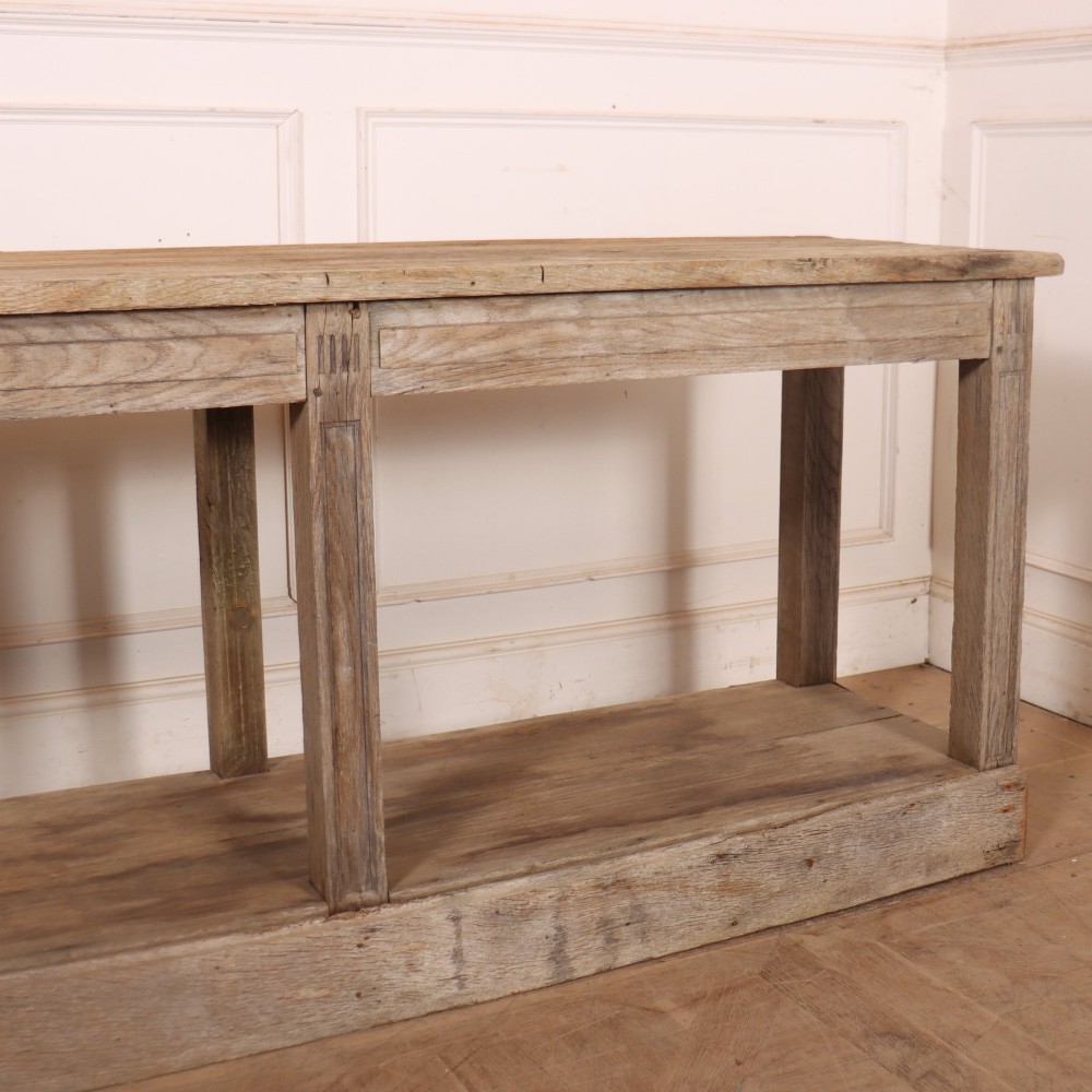 A pair of long rustic wooden French console tables with lower open shelves and weathered pale timber finish. View X