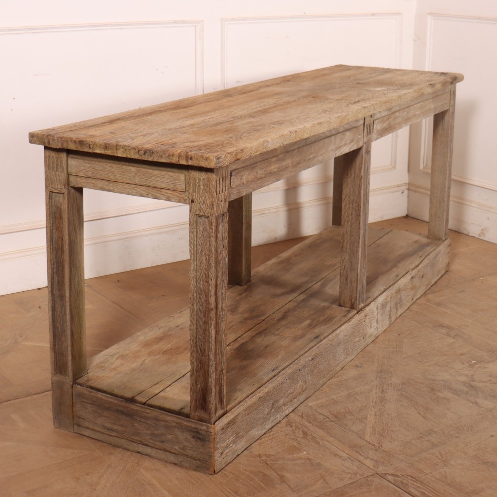 A pair of long rustic wooden French console tables with lower open shelves and weathered pale timber finish. View XI
