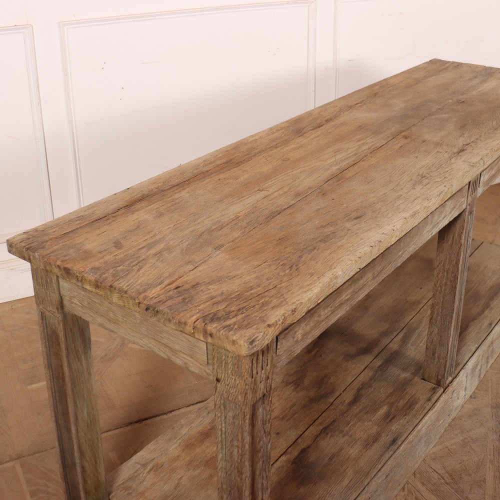 A pair of long rustic wooden French console tables with lower open shelves and weathered pale timber finish. View XII