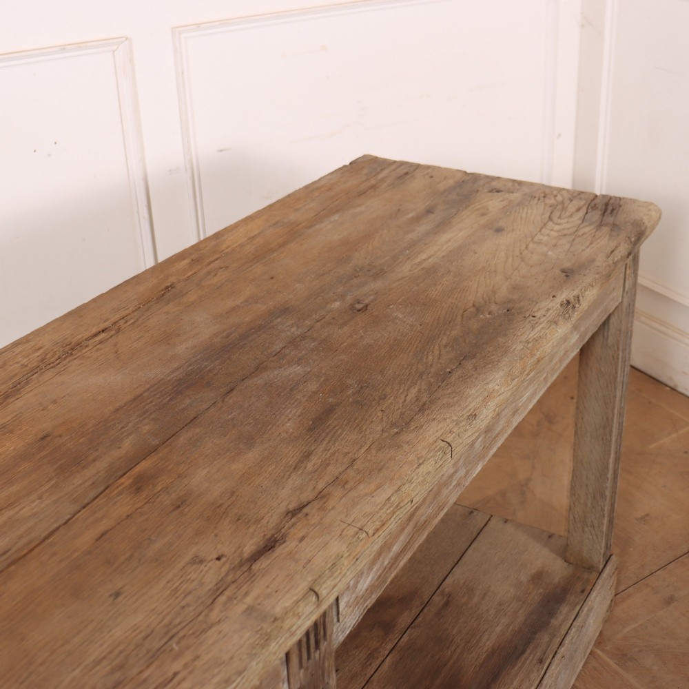 A pair of long rustic wooden French console tables with lower open shelves and weathered pale timber finish. View XIII