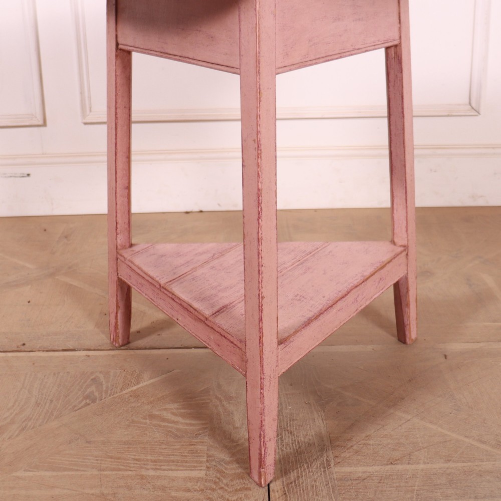 A nineteenth-century cricket table with a round, light natural wood top resting on a three-legged pink painted frame with a triangular lower shelf. View II