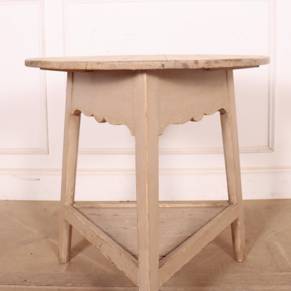A nineteenth-century round wooden cricket table with three tapered legs, a lower triangular shelf, a scalloped apron, and a pale grey painted finish. View III