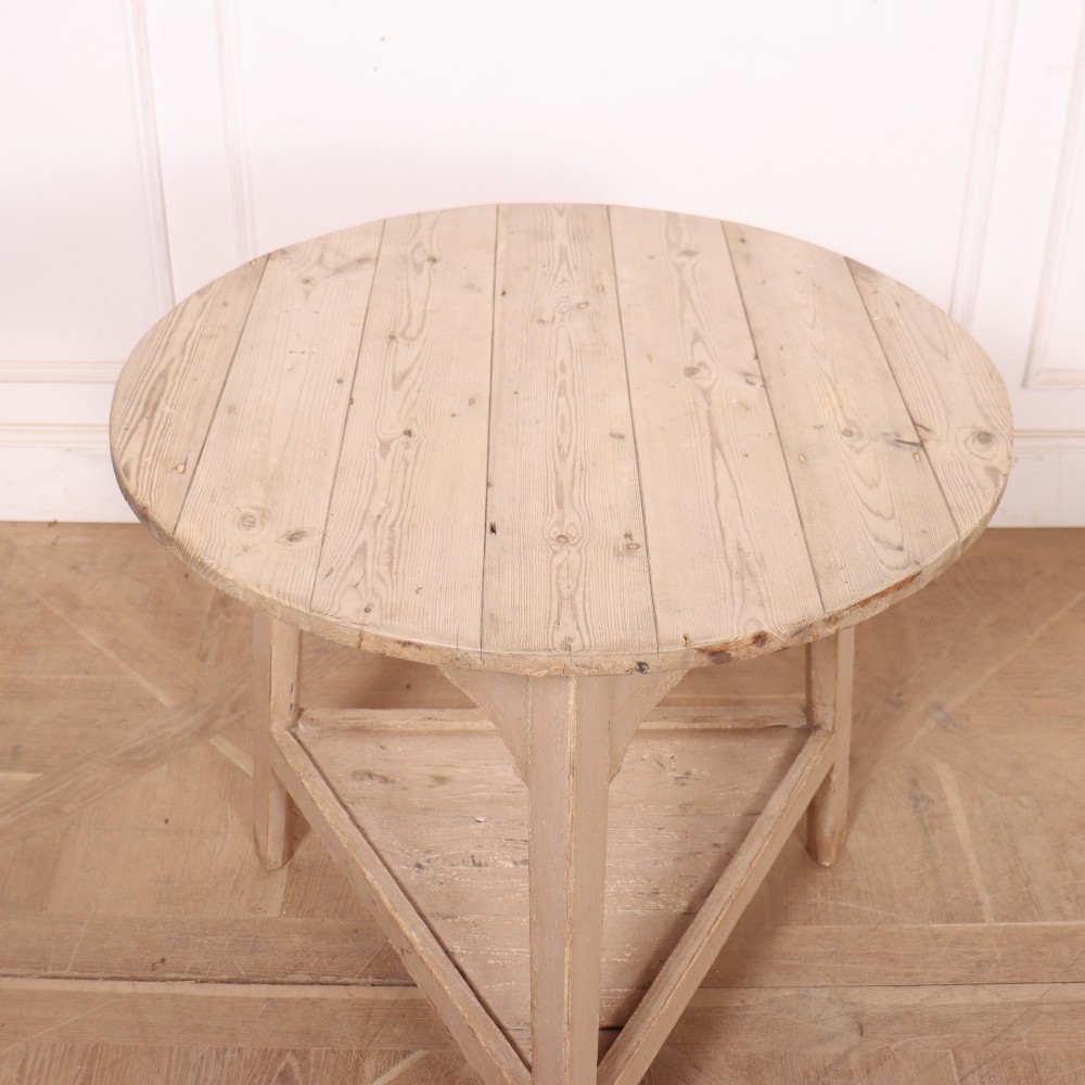 A nineteenth-century round wooden cricket table with three tapered legs, a lower triangular shelf, a scalloped apron, and a pale grey painted finish. View VI