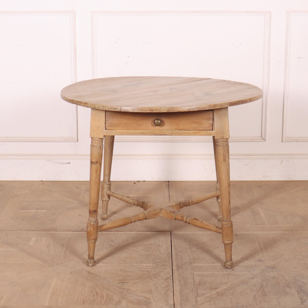 A 19th-century circular Welsh tavern table constructed from light pine with a frieze drawer, turned legs, and an X-frame stretcher.