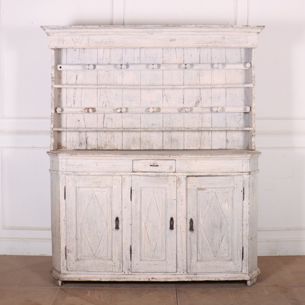 An antique off-white painted Danish pine dresser featuring an open tiered plate rack above a three-door cupboard base with diamond-moulded panels.