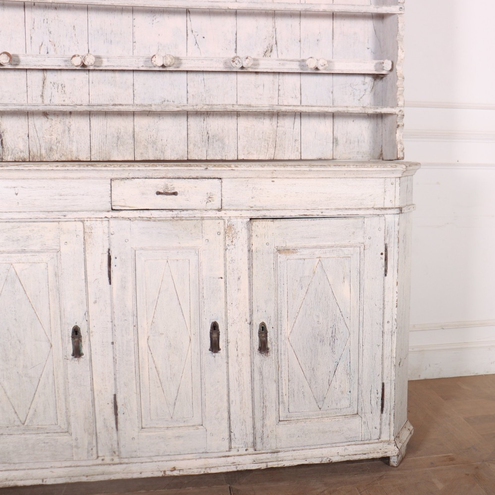 An antique off-white painted Danish pine dresser featuring an open tiered plate rack above a three-door cupboard base with diamond-moulded panels. View III