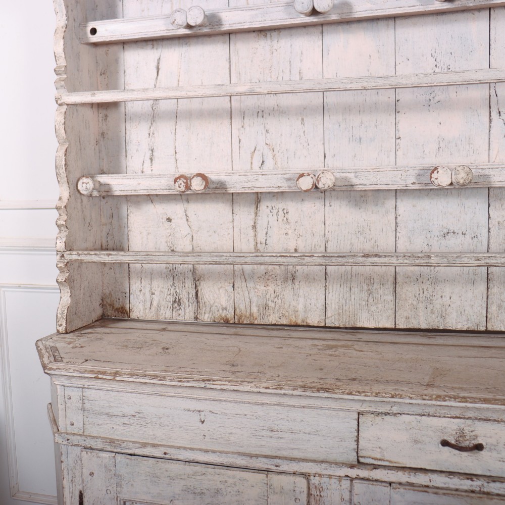 An antique off-white painted Danish pine dresser featuring an open tiered plate rack above a three-door cupboard base with diamond-moulded panels. View V