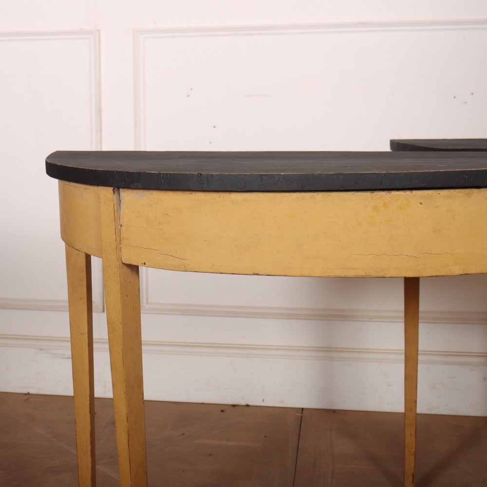 A pair of small painted demi-lune console tables with black tops, ochre yellow bases, and slender square tapered legs. View II