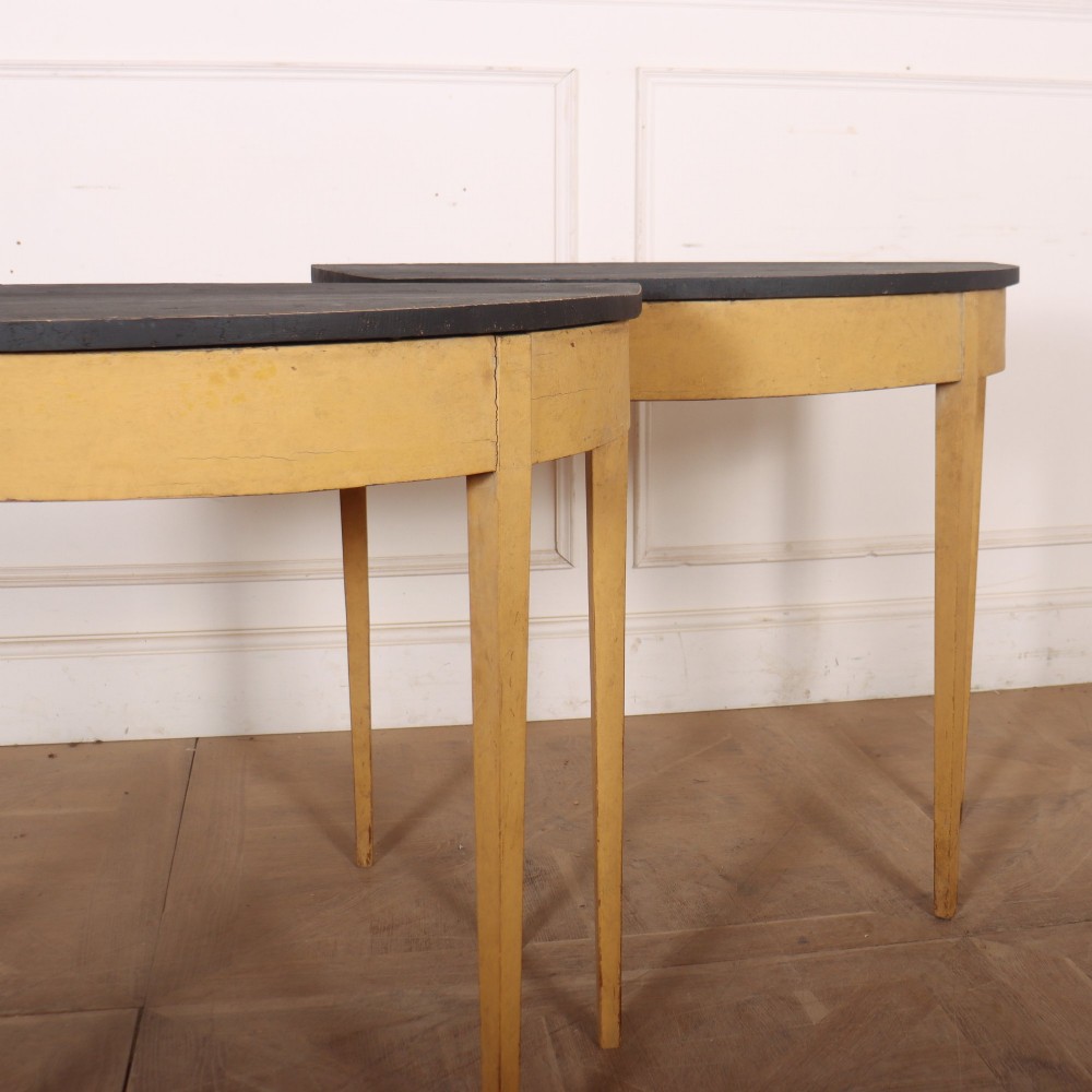 A pair of small painted demi-lune console tables with black tops, ochre yellow bases, and slender square tapered legs. View III