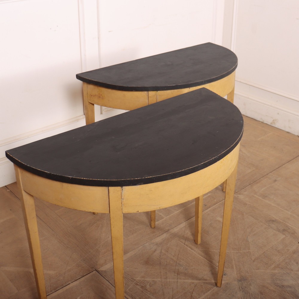 A pair of small painted demi-lune console tables with black tops, ochre yellow bases, and slender square tapered legs. View V