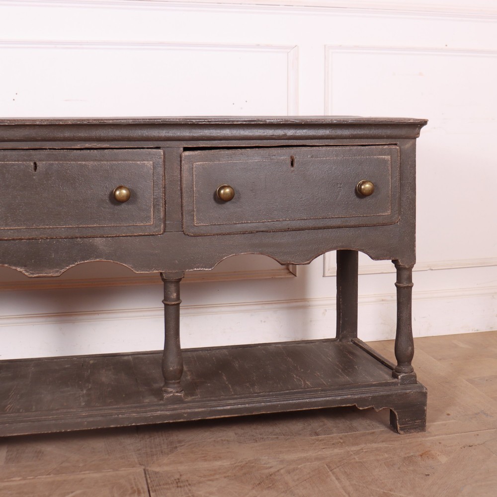 An English painted potboard dresser base in slate grey featuring three frieze drawers with brass handles and a low open shelf supported by turned legs. View IV