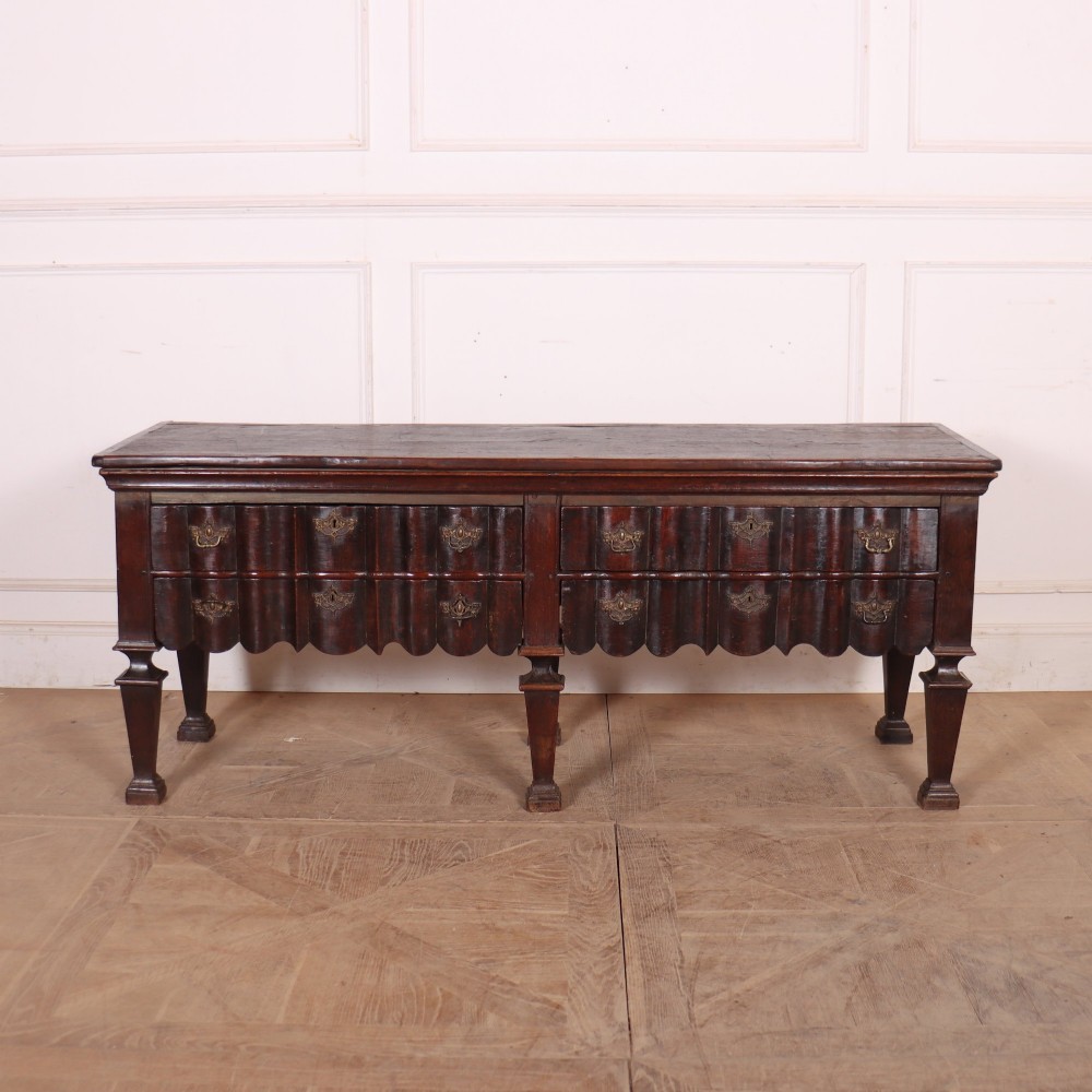 An antique dark oak Dutch dresser base with fluted drawer fronts, brass hardware, and turned legs.