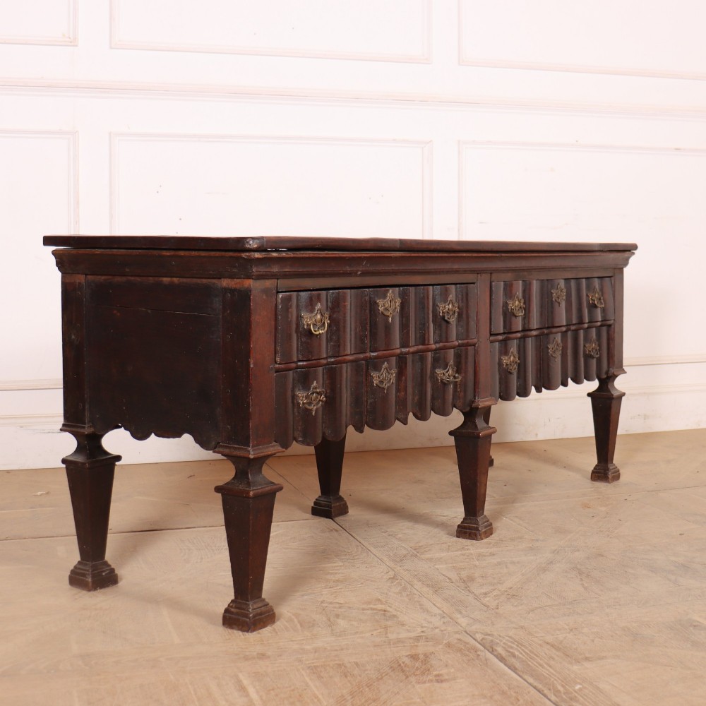 An antique dark oak Dutch dresser base with fluted drawer fronts, brass hardware, and turned legs. View V