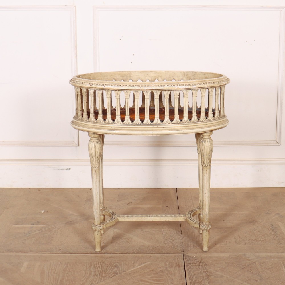 An oval cream painted antique jardiniere table featuring a pierced baluster gallery rim, slender carved legs, and a lower curved stretcher base.