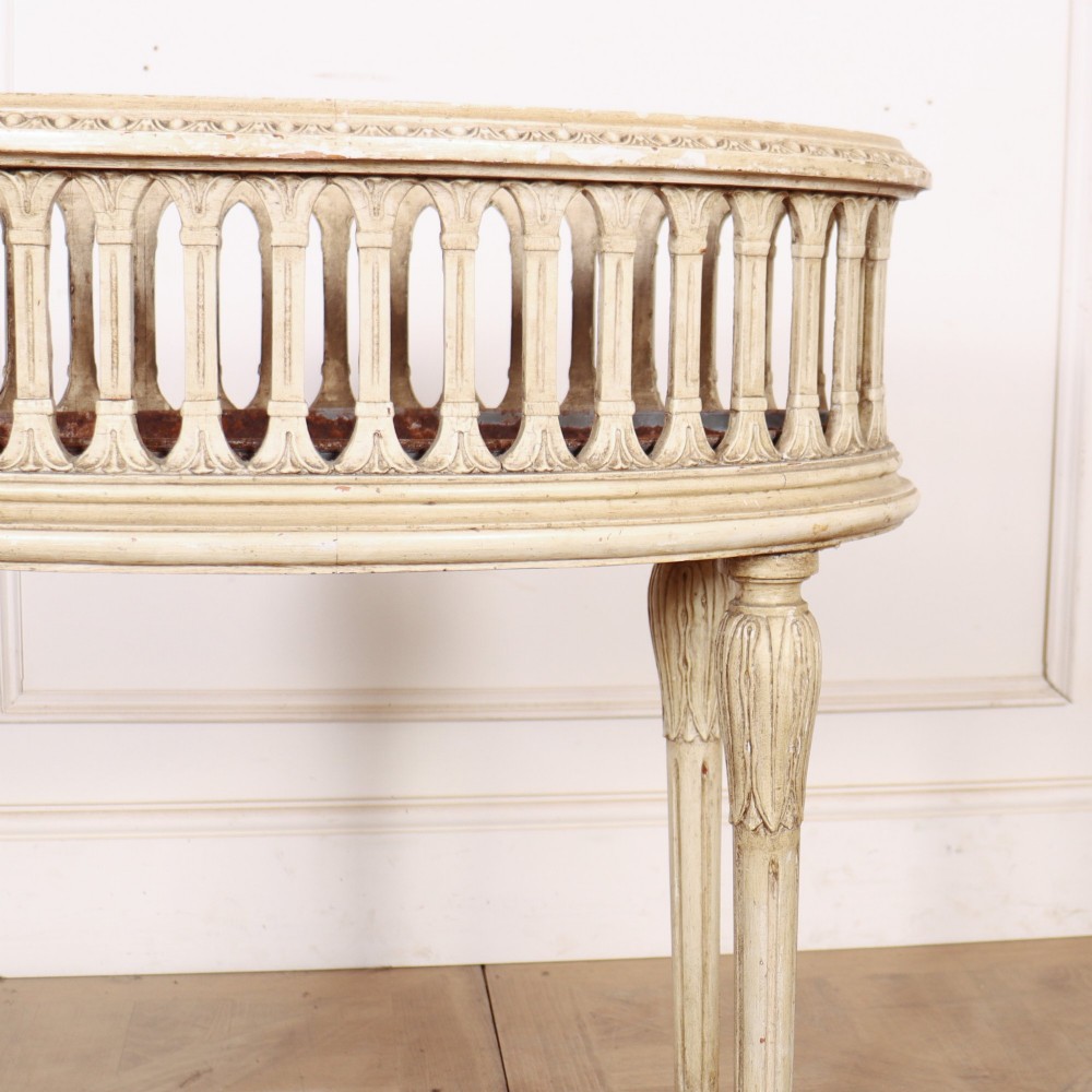 An oval cream painted antique jardiniere table featuring a pierced baluster gallery rim, slender carved legs, and a lower curved stretcher base. View IV