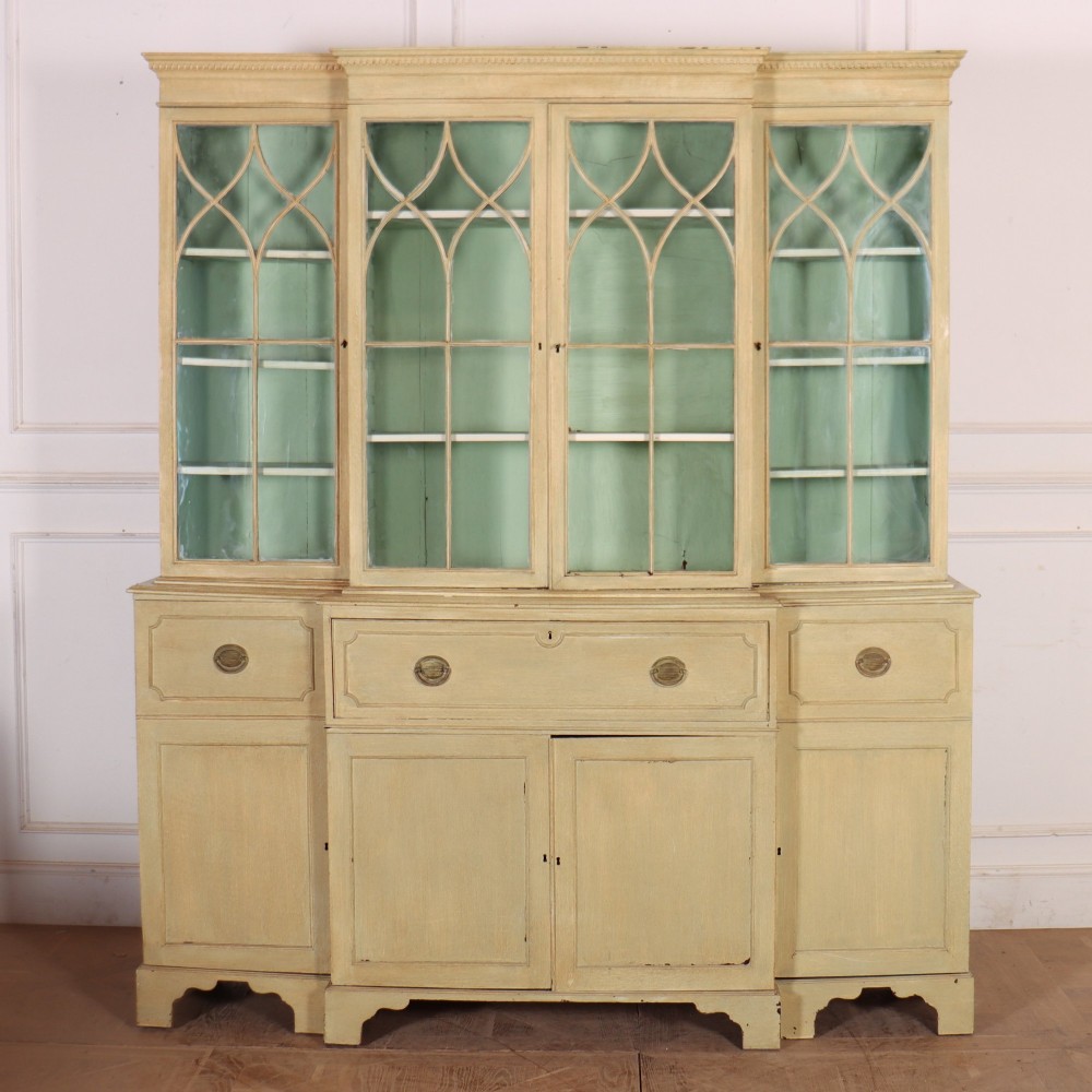 A nineteenth-century painted breakfront secretaire bookcase featuring upper Gothic astragal glazed doors over a green interior backdrop, above lower drawers and panelled cupboard doors.