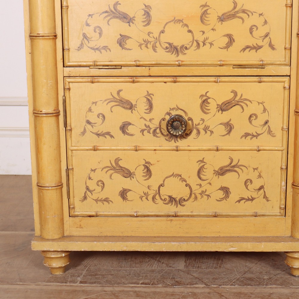 A pair of 19th-century pale yellow painted bedside cabinets featuring turned faux bamboo corner columns and hand-painted foliate motifs. View V