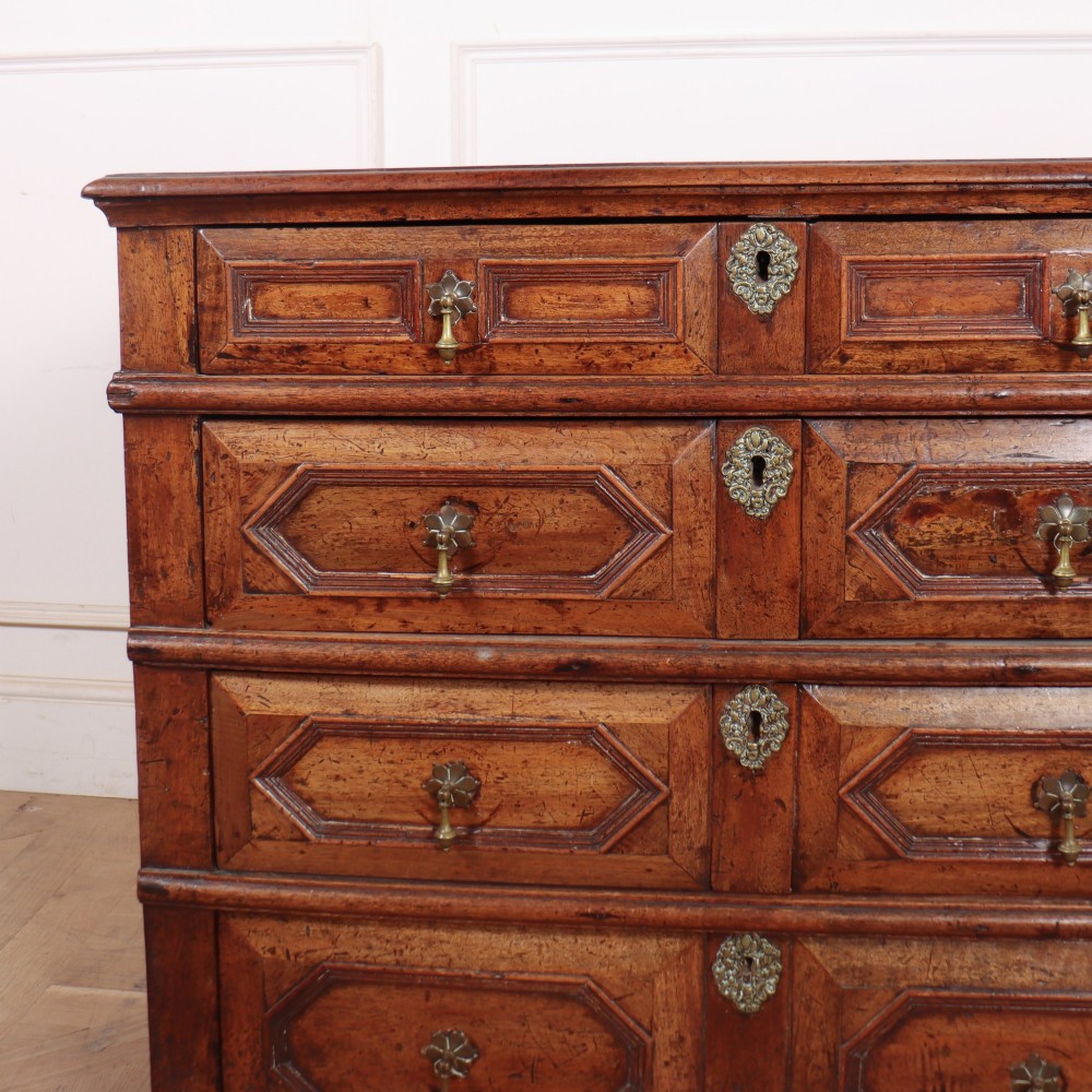 An eighteenth-century oak chest of drawers featuring geometric panelled drawer fronts, brass drop handles, brass escutcheons, and bracket feet. View II